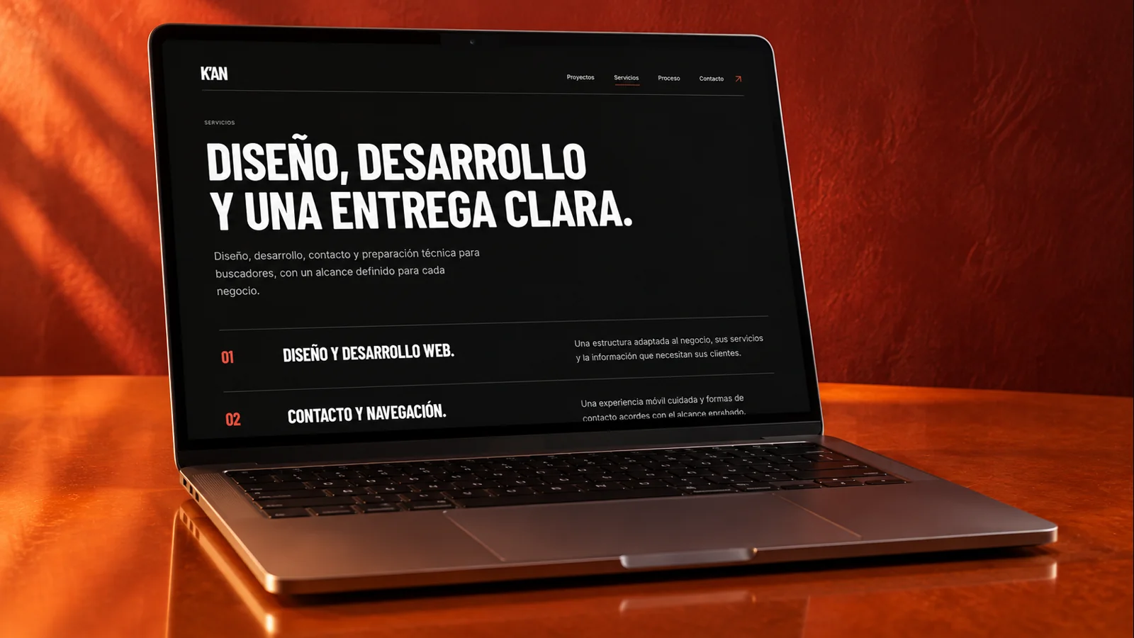 Laptop con la página de servicios de K’AN, sobre una superficie naranja con iluminación cálida. Composición visual original.